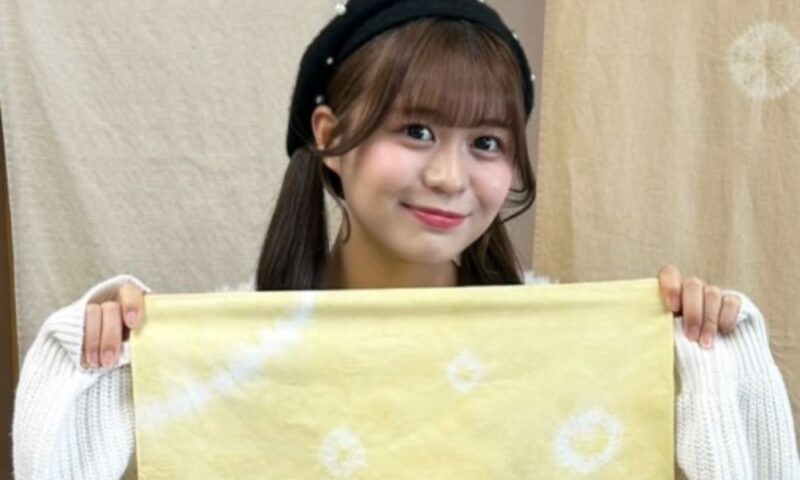 りんご娘の金星が板柳町ふるさとセンターで草木染め体験を行い、りんごの葉や枝で染めた黄色の布を手に笑顔を見せる様子