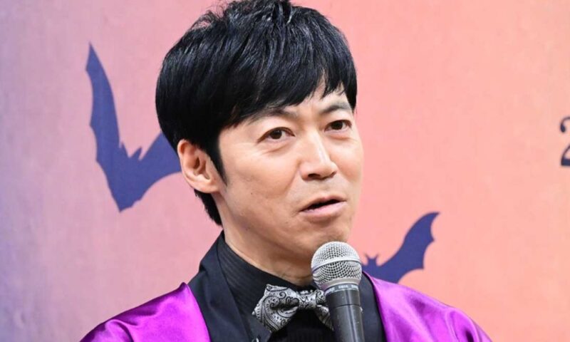 マイクを手にコメントする東貴博、パープルの衣装でイベント登壇中の様子