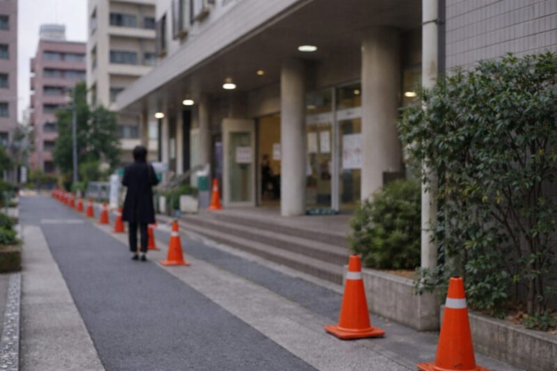 公共施設の入口へ向かう人と整然と並ぶカラーコーンの様子