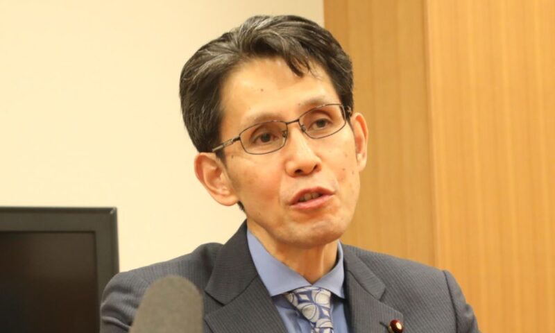 階猛がスーツ姿でインタビューに応じている様子(室内・マイクが手前に見える)