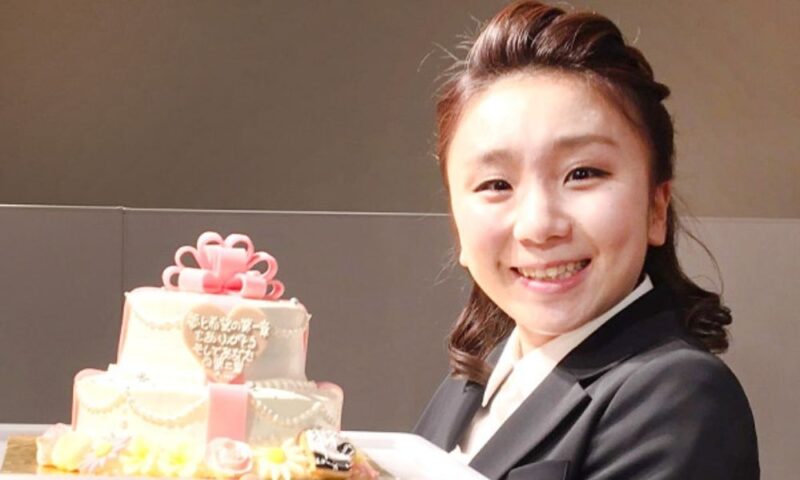 スーツ姿でケーキを手に笑顔を見せる高橋成美さん