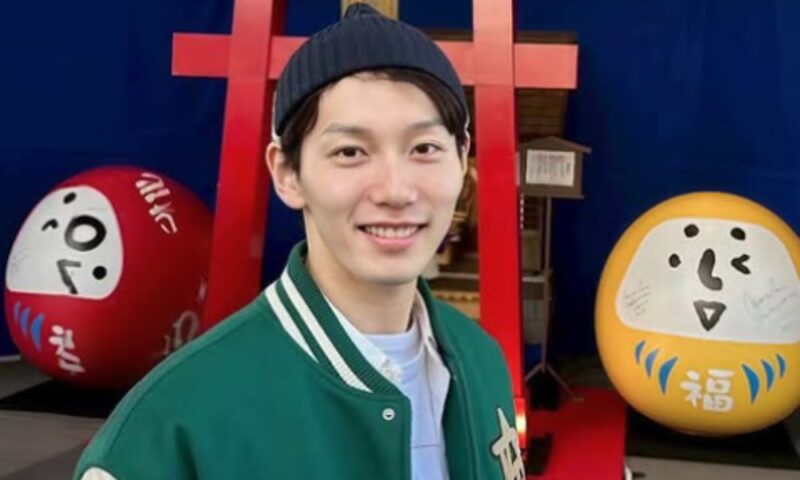 階晴紀が屋内イベント会場で撮影された笑顔の写真(赤い鳥居風オブジェとだるま風装飾が背景)