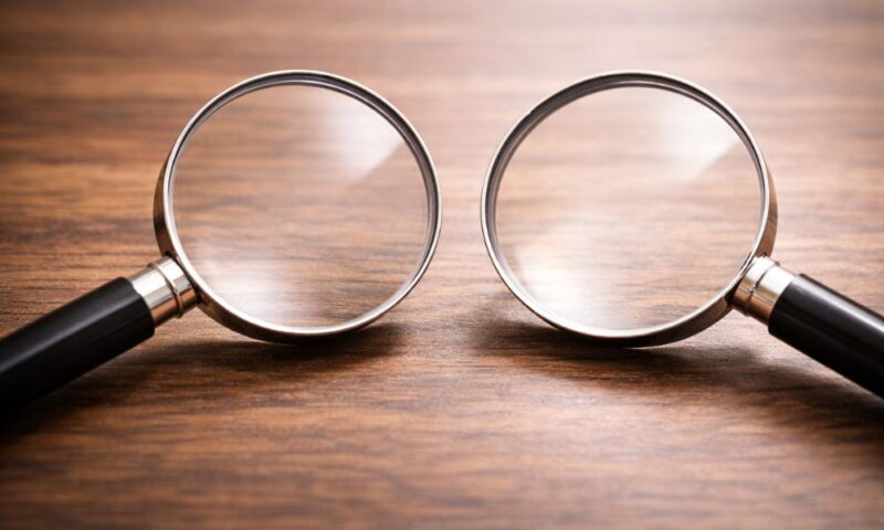 木製テーブルの上に並べられた2つの虫眼鏡、情報の検証や真相解明をイメージしたビジュアル