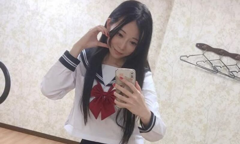芸人いぜんがセーラー服姿でスマートフォンを使い鏡越しに自撮りしている様子