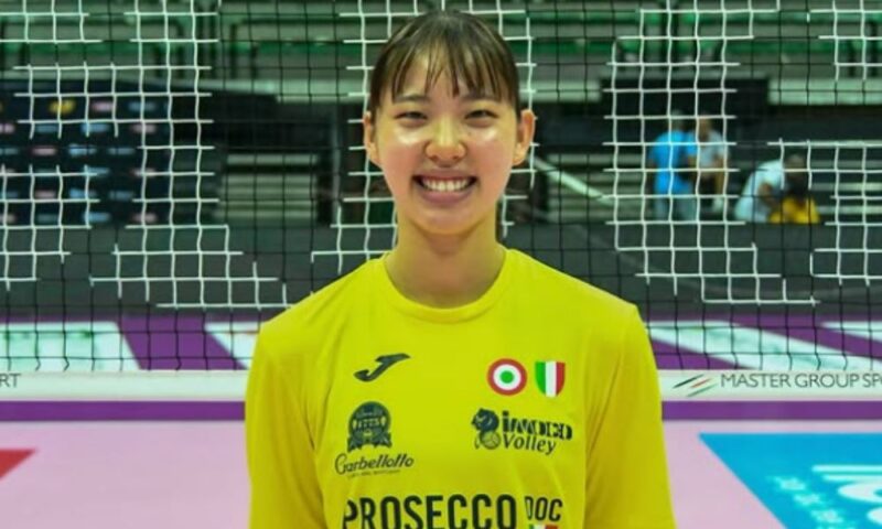 関菜々巳選手がバレーボールコートでユニフォーム姿で笑顔を見せている様子