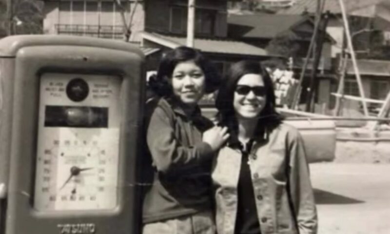 浅野順子の若い頃のモノクロ写真。レトロなガソリンスタンドの計量機の横で笑顔を見せる、10代当時の貴重な姿」