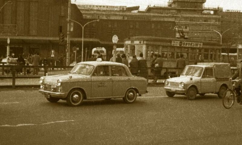 1960年代の横浜駅東口の風景。レトロなトヨペット・クラウンのタクシーや路面電車が走り、当時の活気あふれる街並みを捉えたセピア調の写真