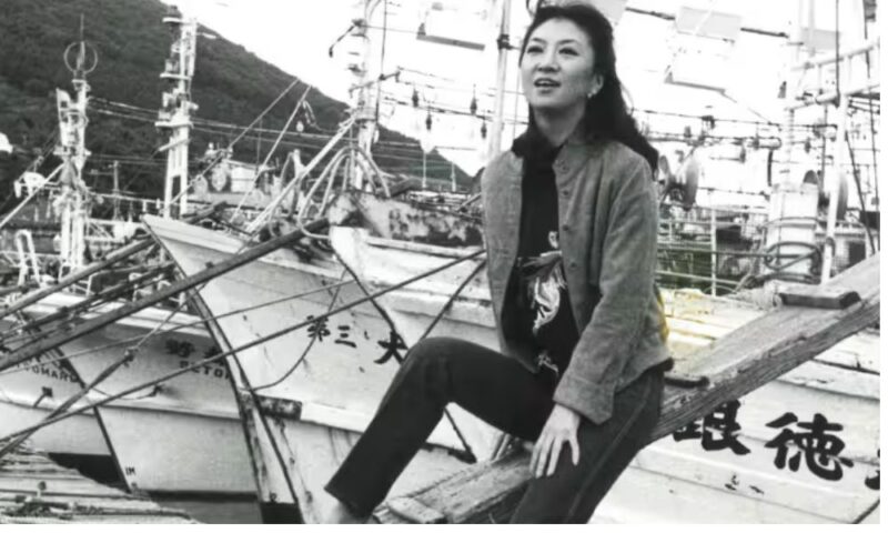若き日の大月みやこが漁港の船の上で微笑むモノクロ写真、初ヒットと初紅白出場の頃をイメージ