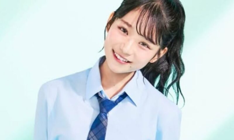 水色のシャツに紺色のチェック柄ネクタイを締めた制服姿の**日向祢音（ひなたねね）**さん。黒髪のポニーテールで、首を少しかしげながらカメラに向かって明るく微笑んでいます。背景は爽やかなライトグリーンと白のグラデーションです。