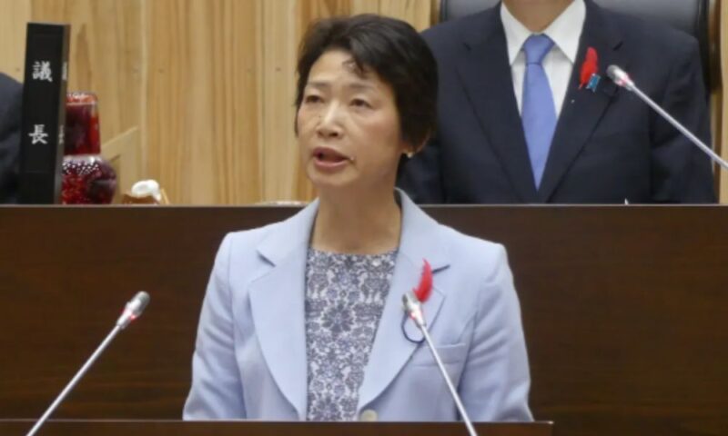 議場で演説する堀江姓の女性議員の写真。水色のジャケット姿で演壇に立っている。記事の堀江ひとみ(1935年生・反暴力団運動)とは別人。