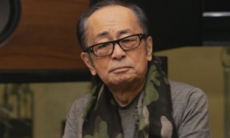 黒縁メガネと迷彩柄のマフラーを身につけ、スタジオにいる大野雄二さん
