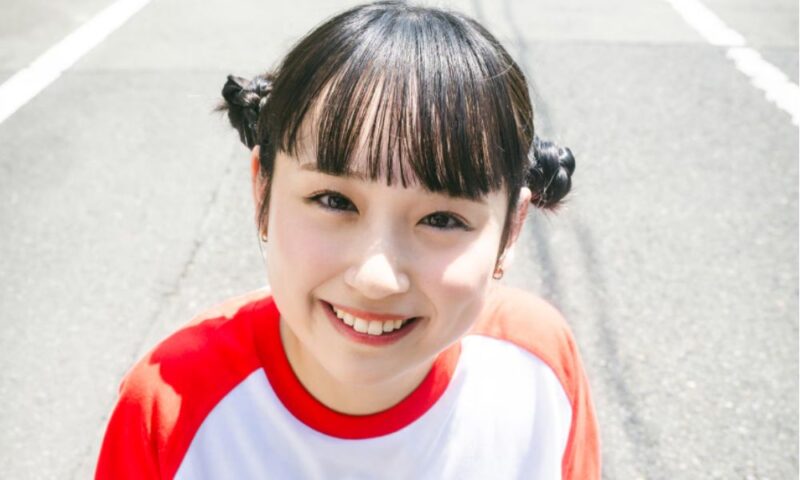 サバシスターのなち。お団子ツインヘアでカメラを上から見上げ、笑顔を見せる様子。