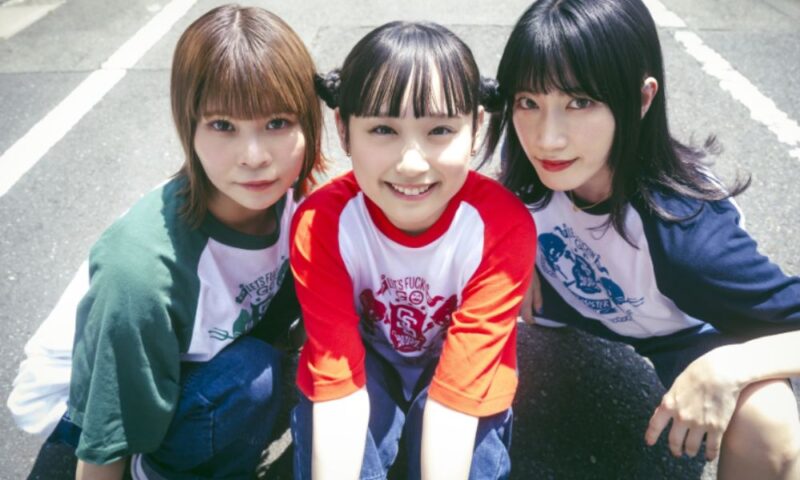 ガールズバンド「サバシスター」のメンバー。中央のなち、左のるみなす、右のGKが並んで笑顔を見せるショット。
