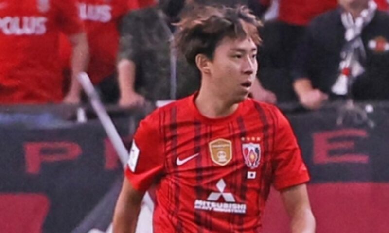 浦和レッズの赤いホームユニフォームを着た柴戸海選手が、試合中に集中した表情でプレーしている様子