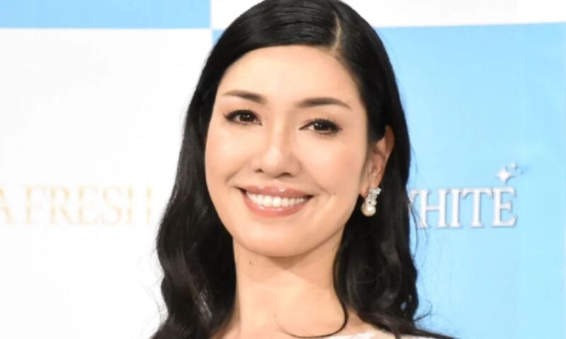 タレント・モデルのアンミカ。黒髪のウェーブヘアに白いレースのトップス、パールのピアス姿で大きく微笑む近影