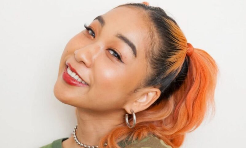 YouTuber・タレントのフワちゃん。オレンジヘアのサイドポニーに迷彩柄Tシャツ、赤いリップで微笑む近影ポートレート