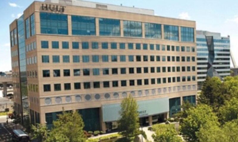 アメリカ・ボストンにある経営大学院 Hult International Business School のキャンパス外観写真。ガラス窓が並ぶベージュ色の中高層ビルの上部に「HULT」のロゴが入り、手前には緑豊かな街路樹と小さな池や芝生が広がっている。